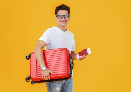 Ethnic young man with luggage smiling and looking at camera on yellow backdrop before summer vacationの写真素材