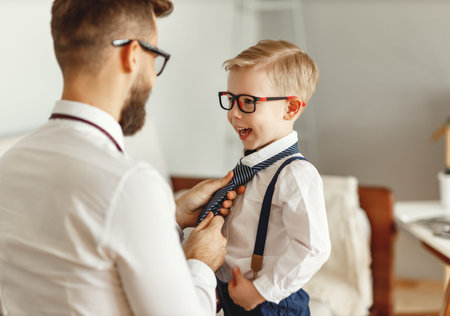 Back view of young man in formal wear and eyeglasses adjusting necktie of cheerful little kid in...