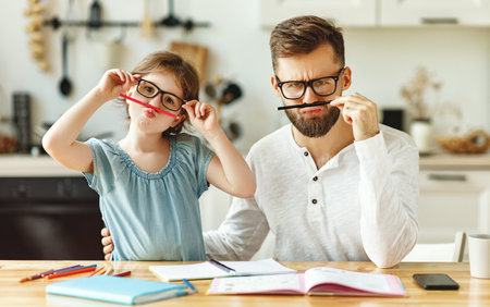 Cheerful schoolgirl with dad wearing similar eyeglasses having fun and looking at camera while...