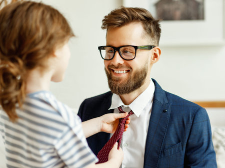 Unrecognizable little girl adjusting tie of happy dad wearing formal suit and eyeglasses during...