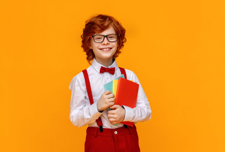 Delighted ginger boy in glasses hugging textbooks and smile broadly during school studies against...