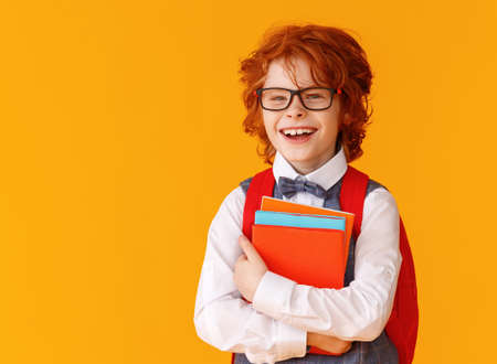 Delighted ginger boy in glasses hugging textbooks and smile broadly during school studies against yellow backgroundの写真素材