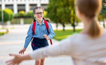 Optimistic girl in glasses smiling and running towards mother after school studies on sunny day