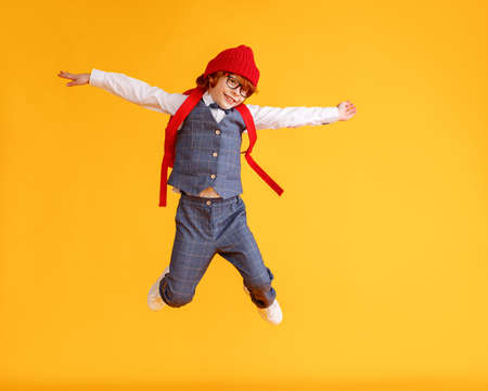 Full length boy in trendy school uniform stretching out arms and jumping against yellow backdropの写真素材