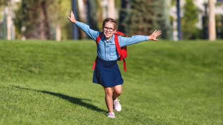 Full body excited girl with backpack stretching out arms and running towards camera while having fun in park after schoolの写真素材
