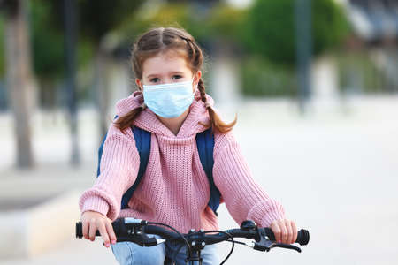 Concept of preventing a coronavirus covid-19 and viral infections. Girl in medical mask goes to school on a bicycleの写真素材