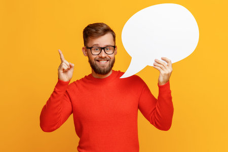 Happy bearded guy smiling and holding blank speech balloon near head against yellow backgroundの写真素材