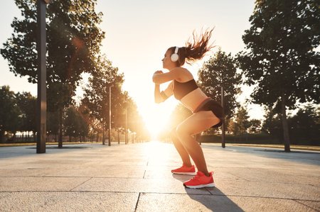 young athletic woman in headphones doing sports squats outdoors