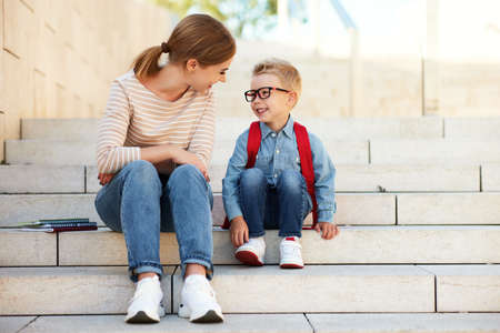 mother and a little son a schoolboy with books and notebooks sit on the stairs together on the first day of schoolの写真素材