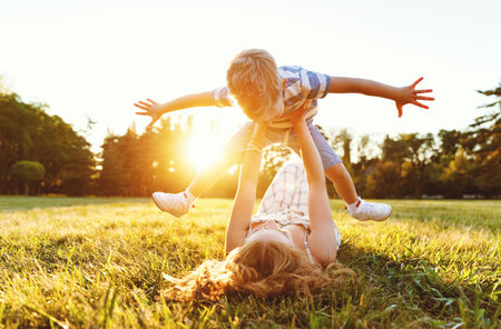 Happy family: mother lying on grass and throwing up cheerful little son in nature in summerの写真素材