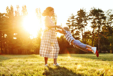Happy family: cheerful mother circles laughing child little son in air in nature in summerの写真素材