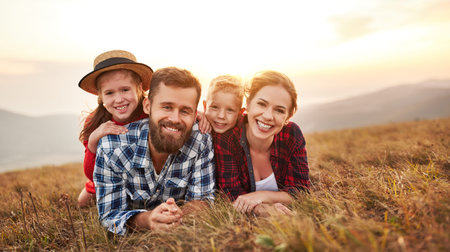 Happy family: mother, father, children son and daughter hugging, laughing and having fun on grass, laughing and playing on nature on sunsetの写真素材
