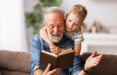 Happy family elderly man and little boy smiling r while sitting on couch and reading fascinating fairy tale together at homeの写真素材