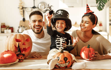 Cheerful multi ethnic family parents with son smiling while creating jack o lantern from pumpkin during Halloween celebration in kitchen at homeの写真素材
