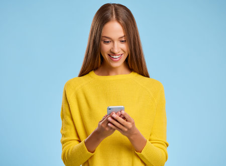 funny cheerful woman in a yellow sweater with smartphone on colored yellow background