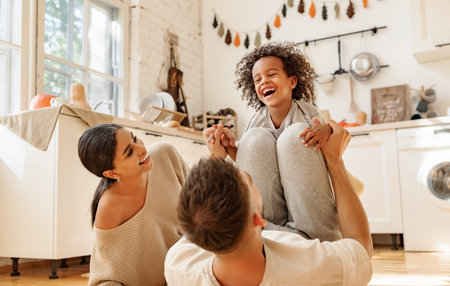 Happy multiracial family: diverse parents playing with son in cozy kitchen on weekend day at home