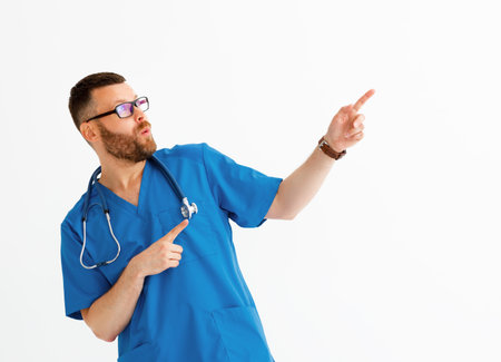 Astonished man in medical uniform and glasses pointing at blank space on white background