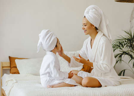 happy family mother and little daughter in dressing gowns and towels laugh and do makeup a Spa day at homeの写真素材