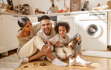 Happy multiethnic family parents and son playing with toy plane on floor in cozy kitchen at home
