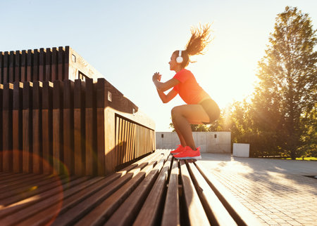 Side view full body of determined young fit female in sportswear and headphones jumping over stairs...
