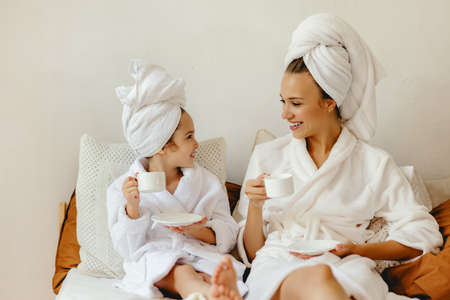 happy family mother and little daughter in bathrobe and towels est and relax with a Cup of coffee in bed at homeの写真素材