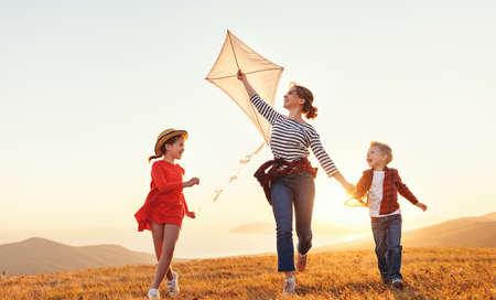 Happy family mother and children launch a kite on nature at sunsetの写真素材