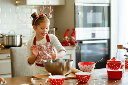 happy funny cute girl bake christmas cookies on cozy kitchen at homeの写真素材