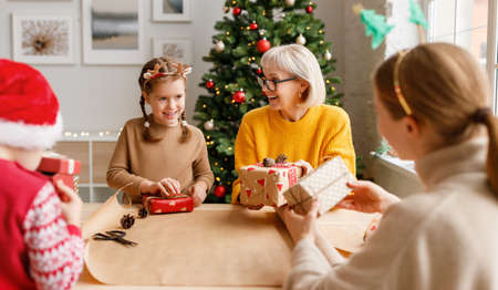 Delighted women and children wrapping Christmas presents together while gathering at table at home and looking at each otherの写真素材