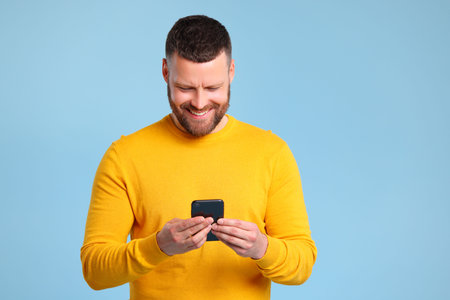 funny cheerful man in a yellow sweater with smartphone on colored blue backgroundの写真素材