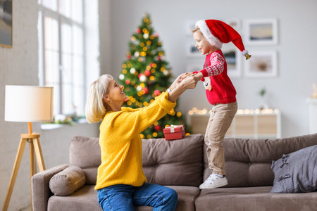 Side view of delighted adult woman and jumping child in Santa hat while having fun at home decorated for Christmas holidaysの写真素材