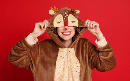 Excited young female smiling and adjusting hood of cute reindeer costume while having fun against red background on Christmas dayの写真素材