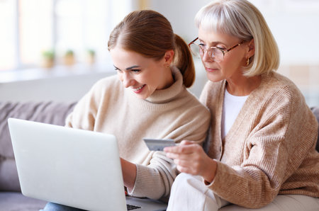 Young daughter and mature mother sitting together with laptop and plastic card while making purchase onlineの写真素材