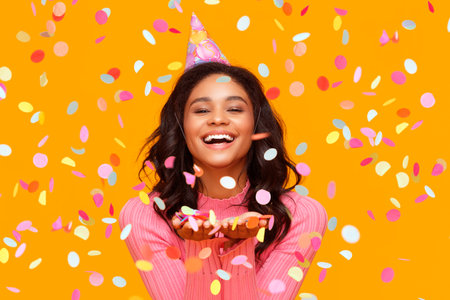 happy birthday! cheerful funny young ethnic woman with festive confetti on yellow backgroundの写真素材