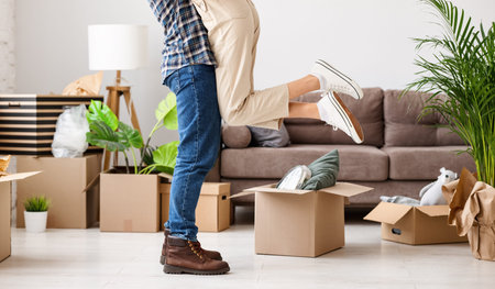 Side view of crop unrecognizable couple hugging in living room with unpacked carton boxes while...