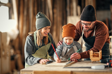 Excited little boy drawing sketch on wooden plank with help of father while spending day with...