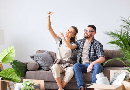 Delighted couple sitting on sofa in new flat with unpacked boxes and dreaming together of living room decoration during relocationの写真素材