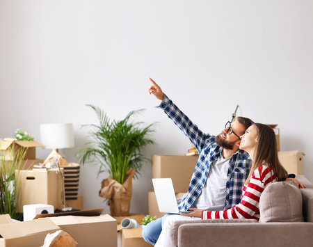 Side view of optimistic married young couple: man with laptop pointing up and discussing design of...