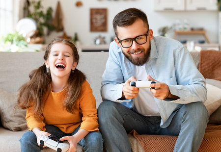 happy family father and daughter laugh and play video games together using a video game console