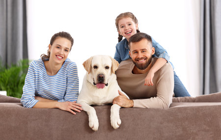 Smiling mother and father with kid daughter and adorable purebred Labrador retriever dog sitting on...