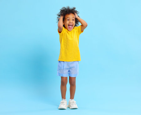 Full length of overjoyed African American little cute boy in casual clothes yelling happily and...