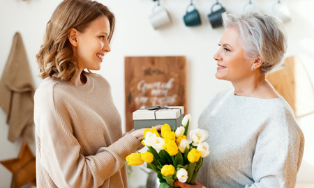 Positive elegant elderly woman with bunch of fresh tulips smiling and accepts a gift from a young daughter during a mother's day celebrationの写真素材