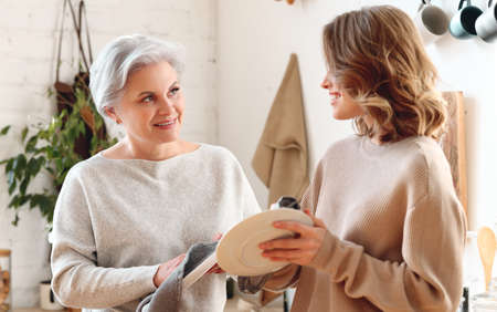 Cheerful young woman hugging aged mother sitting on sofa while resting together in living room at homeの写真素材