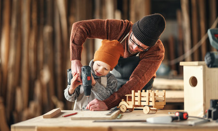 Professional craftsman teaching little son to use drill while making together wooden bird house in carpentry workshopの写真素材