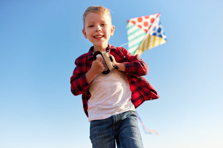 happy kid boy laughing with a kite against the sky outdoors