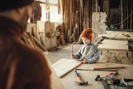 Happy little kid with pencil in hand making marks on wooden plank while assisting father during work...