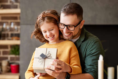 Portrait of young loving father wearing eyeglasses giving his happy cute daughter birthday or christmas present, wrapped gift box with bow, selective focus. Family holidays and celebration conceptの写真素材