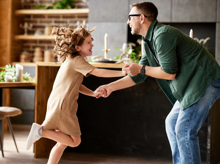 Having fun with daddy. Full leghth of cute excited little girl and young playful father in casual wear dancing and playing together while standing in living room at home. Family leisure activitiesの写真素材
