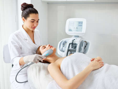 Young relaxed woman receiving professional facial treatment and SMAS lifting with laser machine from cosmetologist in modern beauty salonの写真素材