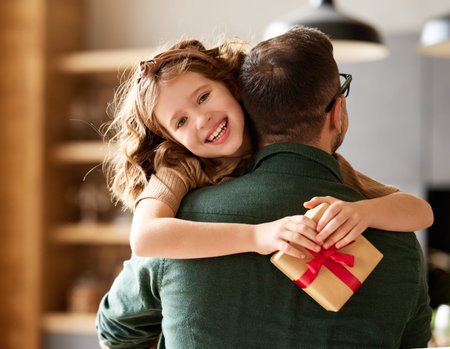 Holidays surprise for beloved daddy. Father receiving wrapped gift box from cute little girl daughter on Fathers day and smiling. Family celebration conceptの写真素材