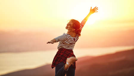 Happy woman with open hands dances, jump, rejoices, laughs on sunset in natureの写真素材